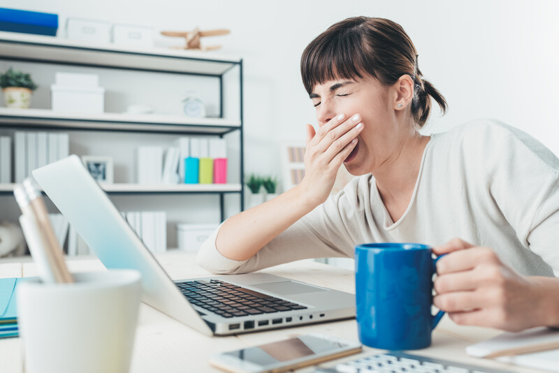Women yawning and tired at her computer with a cup of coffee